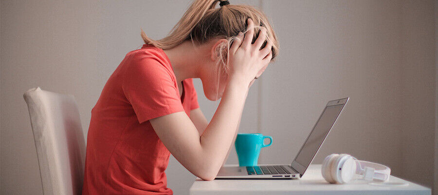 Vrouw met handen in het haar achter een laptop